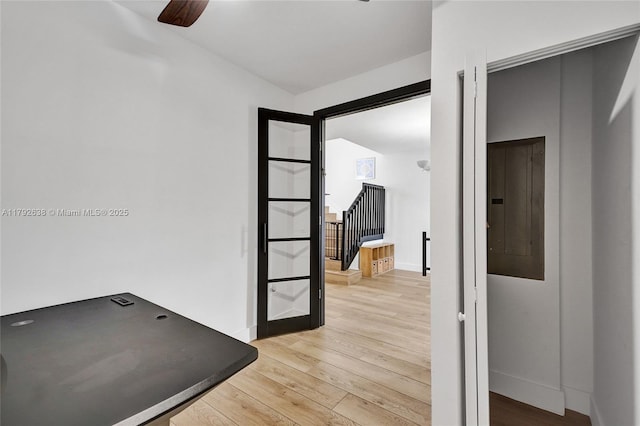 corridor with baseboards, electric panel, and light wood-type flooring