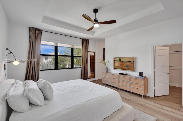 bedroom featuring a ceiling fan, baseboards, a raised ceiling, and light wood-style floors