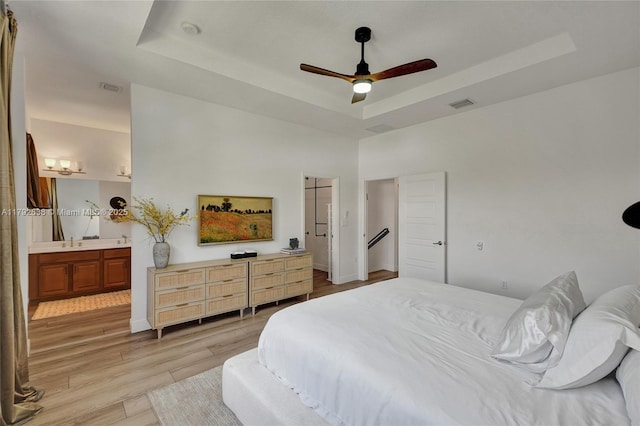 bedroom featuring a raised ceiling, ensuite bathroom, light wood-type flooring, and visible vents