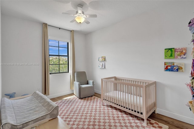 bedroom with baseboards, a crib, ceiling fan, and wood finished floors