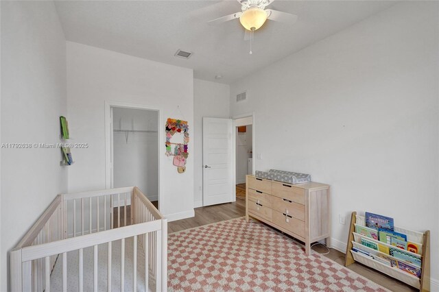 bedroom with ceiling fan, visible vents, wood finished floors, baseboards, and a closet