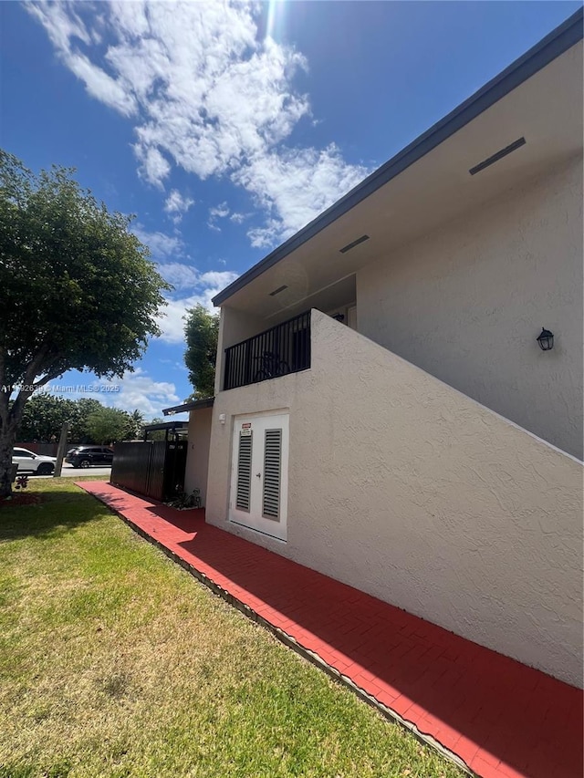 view of property exterior with a lawn, french doors, and stucco siding