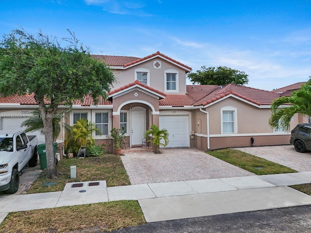 mediterranean / spanish-style home with a garage, stucco siding, driveway, and a tile roof