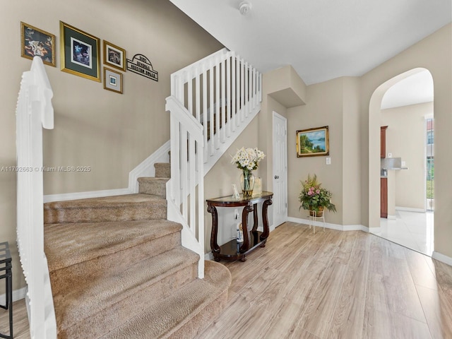 stairs with baseboards, arched walkways, and wood finished floors