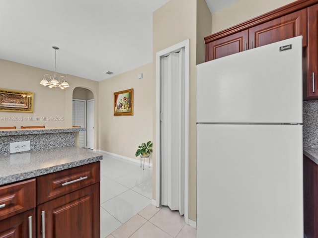 kitchen with freestanding refrigerator, light tile patterned flooring, baseboards, reddish brown cabinets, and arched walkways