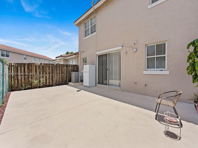 rear view of house featuring fence, central AC unit, stucco siding, and a patio