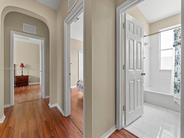 hallway featuring arched walkways, baseboards, visible vents, and wood finished floors