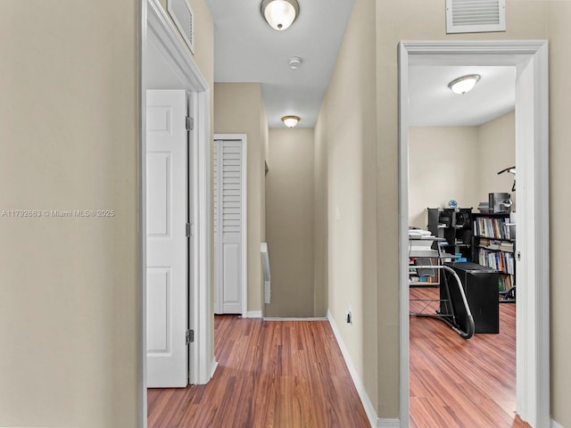hall featuring baseboards, visible vents, and wood finished floors