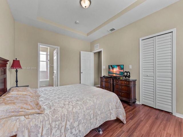 bedroom with visible vents, a raised ceiling, dark wood-type flooring, and a closet