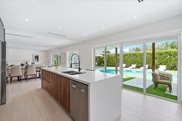 kitchen with modern cabinets, a center island with sink, dishwasher, a sink, and light countertops