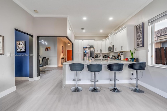 kitchen featuring stainless steel appliances, ornamental molding, a peninsula, and light wood-type flooring