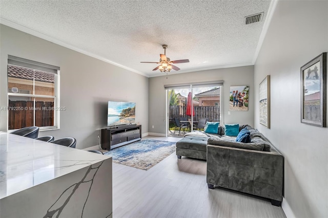 living room featuring a ceiling fan, visible vents, ornamental molding, and wood finished floors