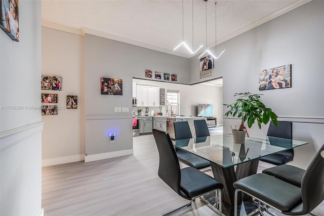 dining space featuring baseboards, ornamental molding, light wood finished floors, and a textured ceiling