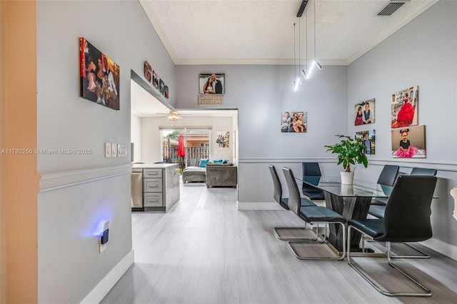 dining area with a textured ceiling, visible vents, crown molding, baseboards, and light wood-style floors