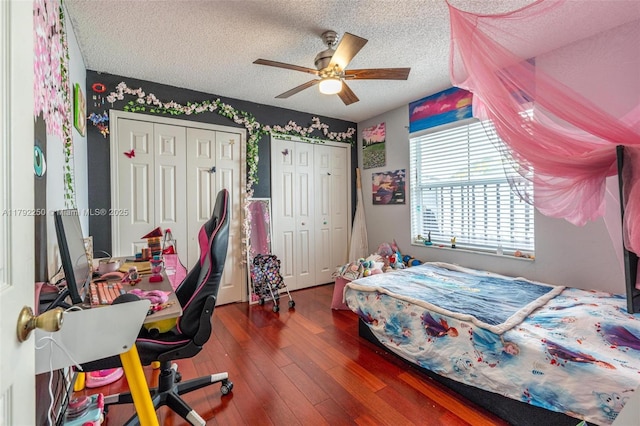 bedroom with a textured ceiling, multiple closets, a ceiling fan, and hardwood / wood-style floors