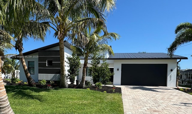 view of front of house featuring an attached garage, a front lawn, stucco siding, decorative driveway, and a standing seam roof