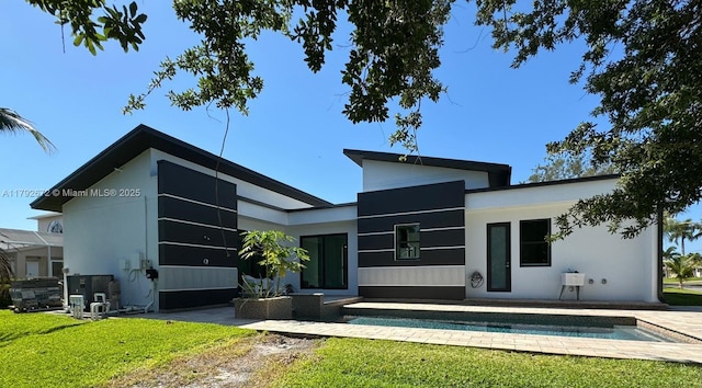 back of house featuring a lawn, a patio, stucco siding, and an outdoor pool