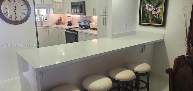 kitchen with a sink, light countertops, a kitchen breakfast bar, white cabinetry, and range with electric stovetop