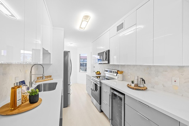 kitchen with appliances with stainless steel finishes, a sink, beverage cooler, light wood-type flooring, and modern cabinets