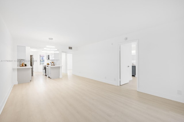 unfurnished living room featuring baseboards, visible vents, and light wood finished floors