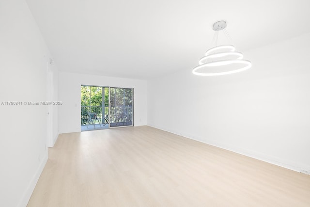 unfurnished room featuring baseboards, light wood-style flooring, and a notable chandelier