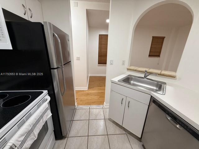 kitchen with stainless steel dishwasher, light countertops, white cabinetry, arched walkways, and a sink