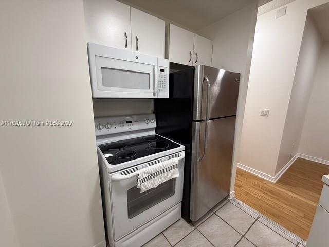 kitchen featuring baseboards, light tile patterned flooring, white cabinets, and white appliances