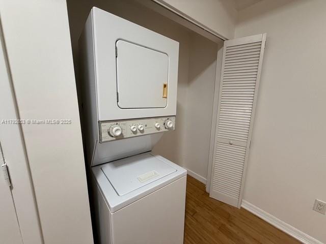laundry room with baseboards, stacked washer and clothes dryer, wood finished floors, and laundry area