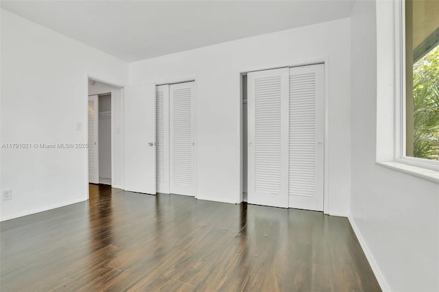 unfurnished bedroom with wood finished floors, two closets, and multiple windows