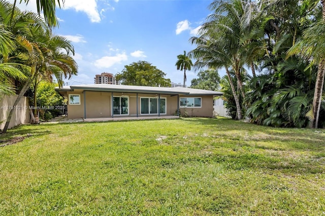 rear view of house with a yard, fence, and stucco siding