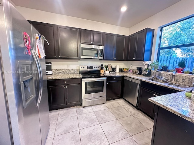 kitchen with light stone counters, a sink, appliances with stainless steel finishes, and light tile patterned flooring