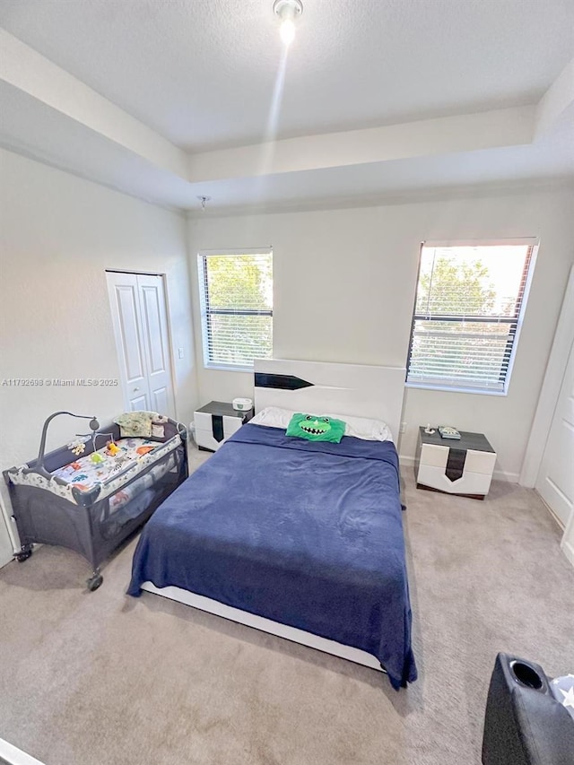 carpeted bedroom with a closet, a textured ceiling, baseboards, and a tray ceiling