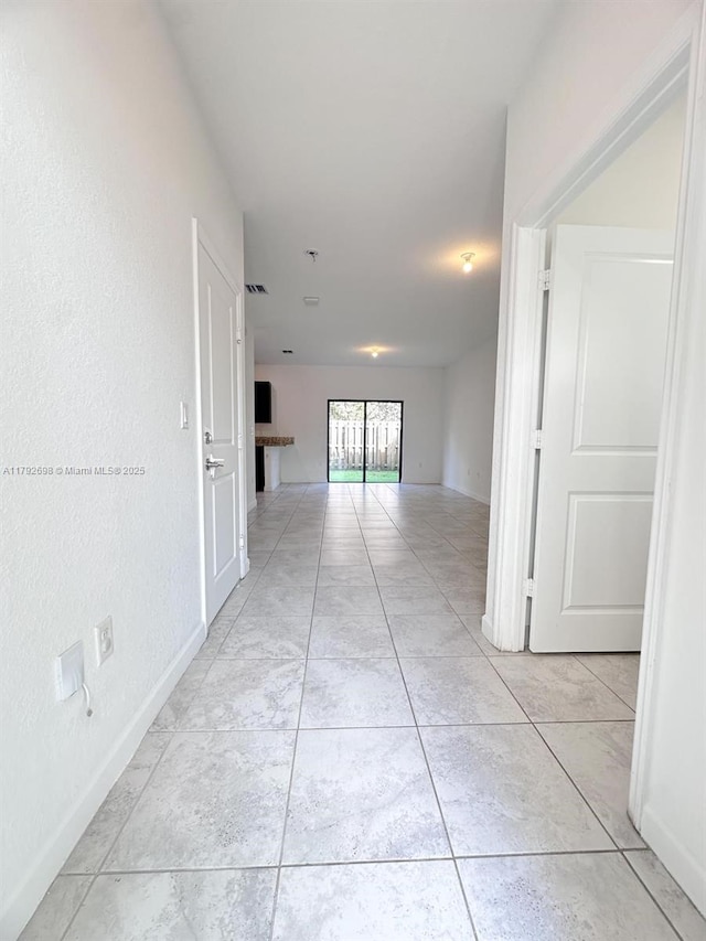 hallway featuring visible vents, baseboards, and light tile patterned flooring