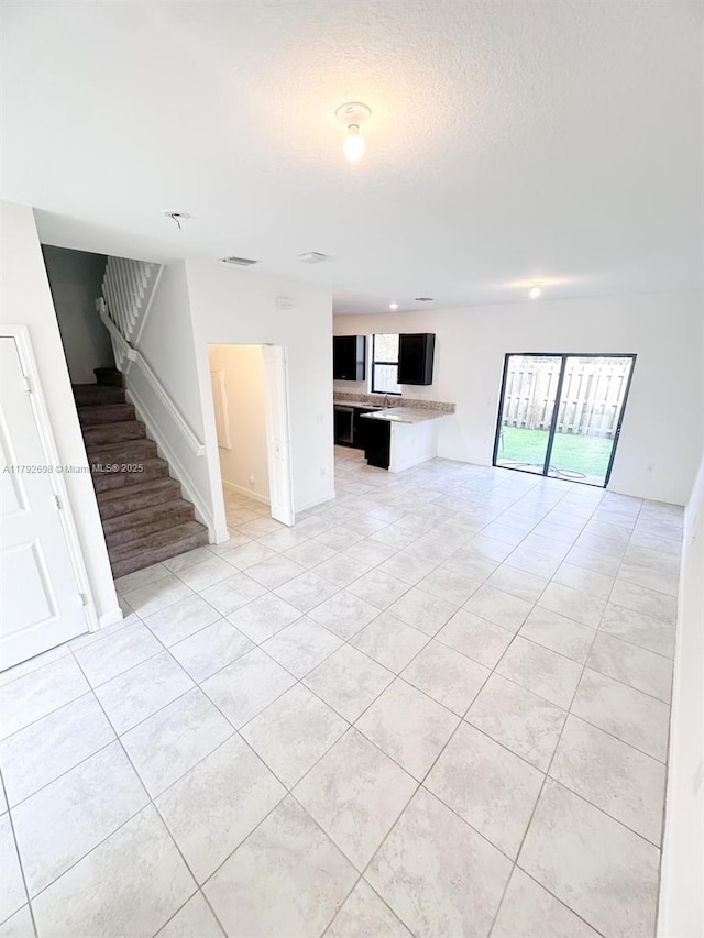 unfurnished living room with plenty of natural light, a textured ceiling, stairs, and light tile patterned flooring