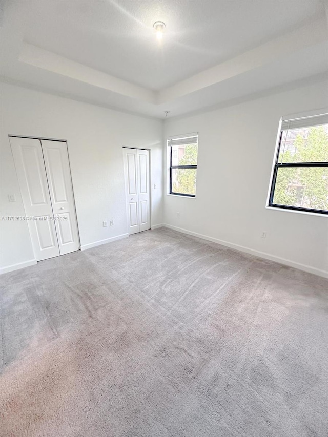 unfurnished bedroom featuring multiple closets, baseboards, a tray ceiling, and carpet floors