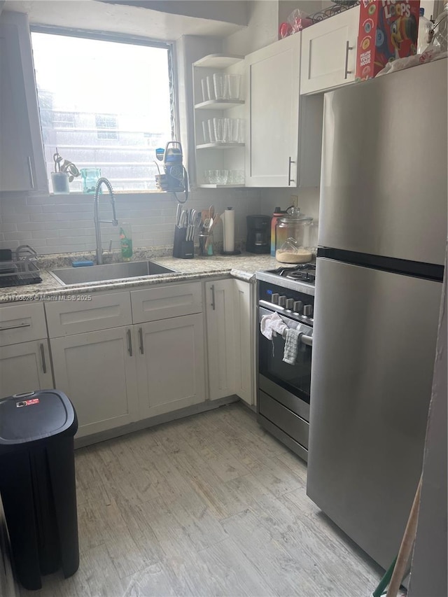 kitchen featuring appliances with stainless steel finishes, tasteful backsplash, open shelves, light wood-type flooring, and a sink