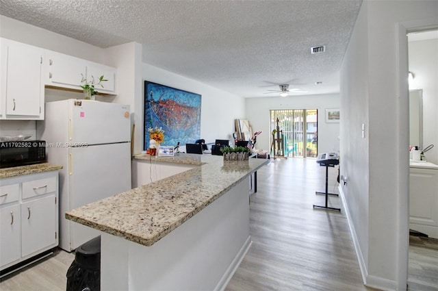 kitchen with visible vents, freestanding refrigerator, a textured ceiling, a ceiling fan, and light wood finished floors