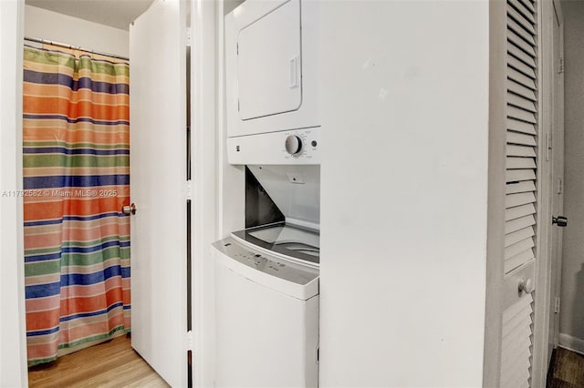clothes washing area featuring stacked washer and clothes dryer, light wood-style flooring, and laundry area