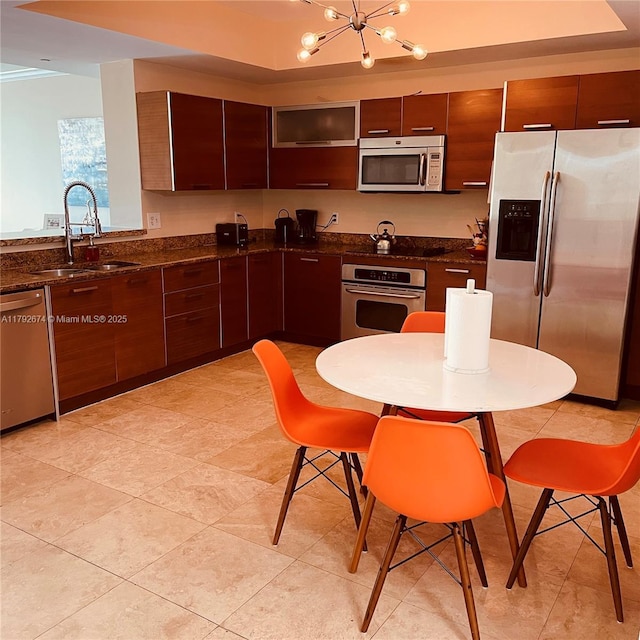 kitchen with appliances with stainless steel finishes, an inviting chandelier, a sink, dark stone counters, and modern cabinets