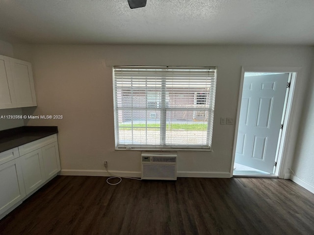 unfurnished dining area featuring baseboards, a textured ceiling, an AC wall unit, and dark wood-style floors