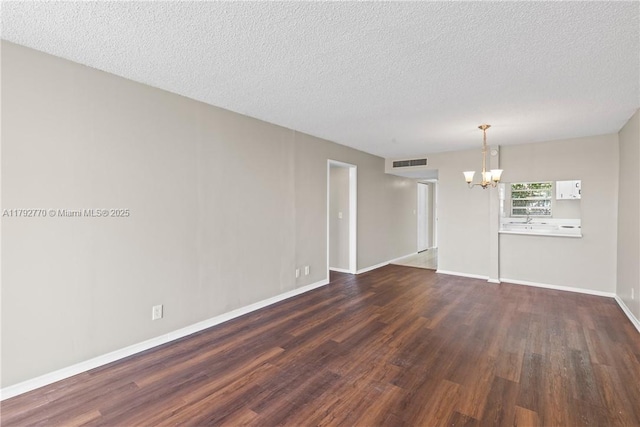 spare room with a textured ceiling, visible vents, baseboards, a chandelier, and dark wood-type flooring