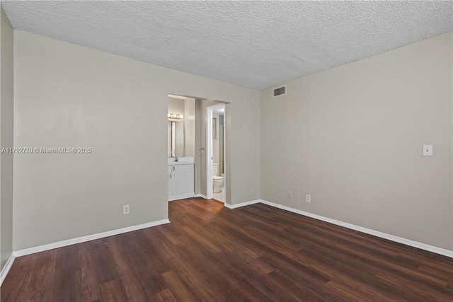 spare room with visible vents, a textured ceiling, baseboards, and wood finished floors