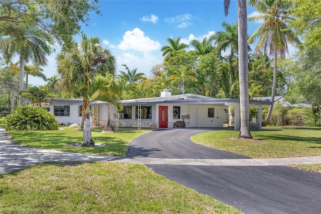 ranch-style home with a chimney, an attached carport, driveway, and a front lawn