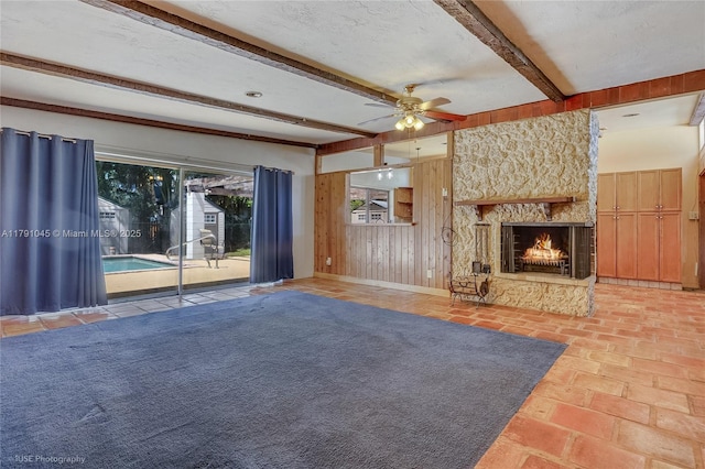 unfurnished living room with wooden walls, beamed ceiling, ceiling fan, and a fireplace