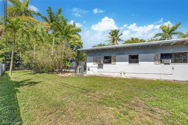 rear view of property featuring central AC, fence, cooling unit, stucco siding, and a yard