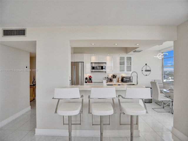 kitchen featuring a breakfast bar, freestanding refrigerator, white cabinetry, visible vents, and glass insert cabinets