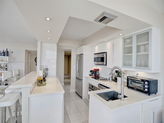 kitchen with appliances with stainless steel finishes, a sink, a toaster, a peninsula, and light tile patterned flooring