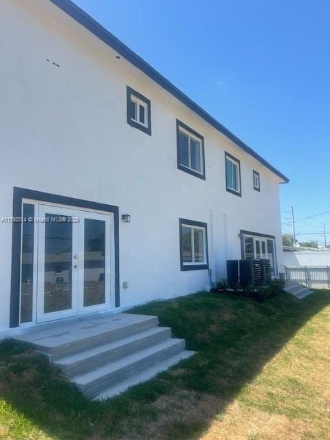 rear view of property with a yard, stucco siding, french doors, and fence
