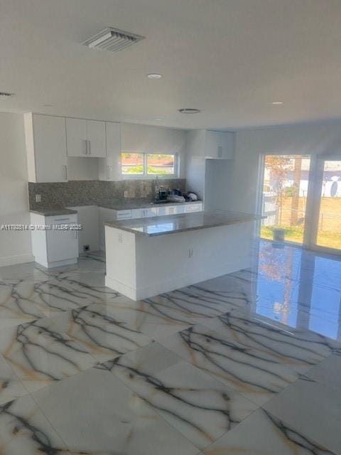kitchen featuring a kitchen island, backsplash, visible vents, white cabinets, and marble finish floor