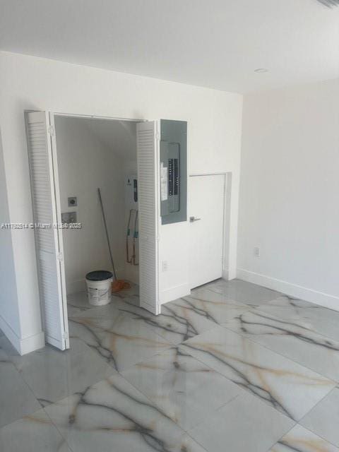 empty room with baseboards, marble finish floor, and electric panel